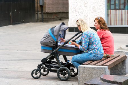 SAMARA, RUSSIA - JUNE 19, 2018: Women with a baby carriage sitting on a bench