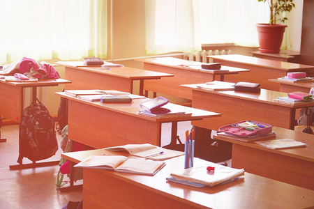 An empty classroom with textbooks, pencils and teaching materials lying on its desksの写真素材