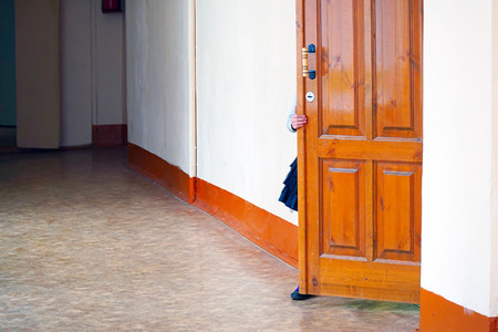Girl opening the door, looks in class. Empty school corridorの写真素材