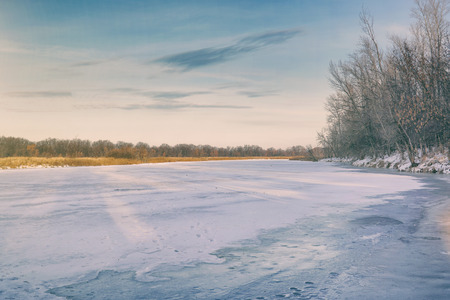 Winter landscape. Frozen river, forest in the distance, dry sedge and blue cloudy skyの写真素材