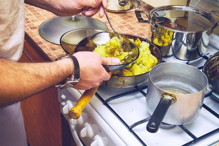 A man in the kitchen puts roast potatoes in a plate