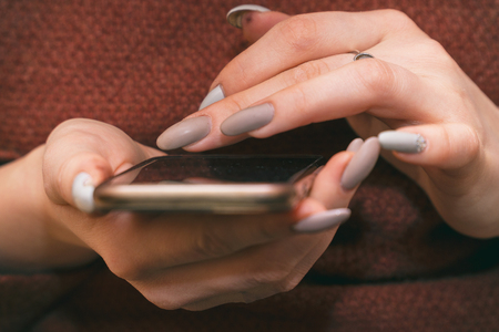 The girl touches her fingers to the phone screen. The girl has a manicure with false nailsの写真素材