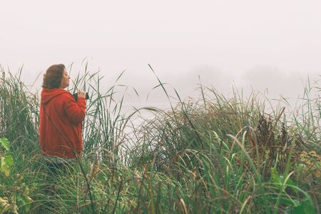 Woman photographer photographs the fog on the lakeの写真素材