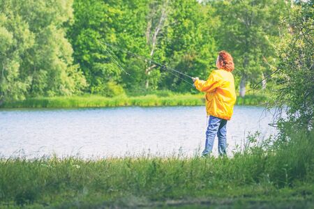 Woman in yellow jacket fishing spinning on the lakeの写真素材