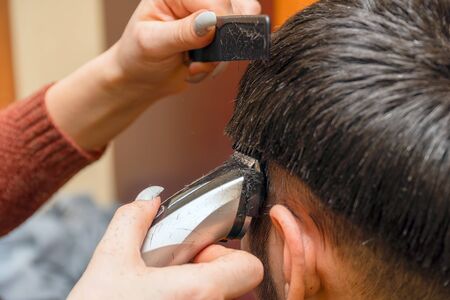 Woman Hairdresser cuts mans hair with electric clipper trimmer. Selective focusの写真素材