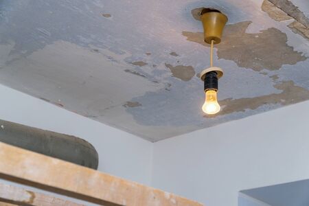 Light bulb hanging on the background of shabby ceiling, requiring repairの写真素材