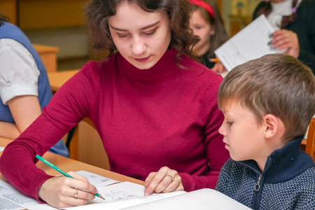 Chapaevsk, Samara region, Russia - October 15, 2019: Elementary school in Chapaevsk. Schoolboy at a desk with a woman teacher. The teacher is engaged with a primary school student. Selective focusのeditorial素材