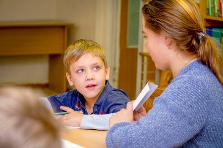 Chapaevsk, Samara region, Russia - October 15, 2019: Elementary school in Chapaevsk. Schoolboy at a desk with a woman teacher. The teacher is engaged with a primary school student. Selective focusのeditorial素材
