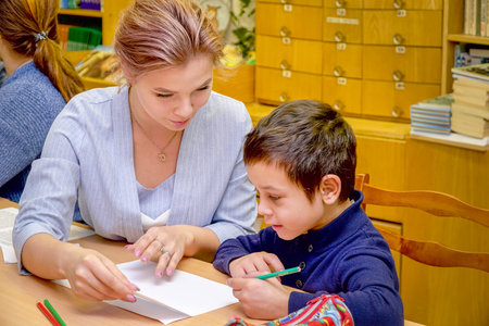 Chapaevsk, Samara region, Russia - October 15, 2019: Elementary school in Chapaevsk. Schoolboy at a desk with a woman teacher. The teacher is engaged with a primary school student. Selective focusのeditorial素材