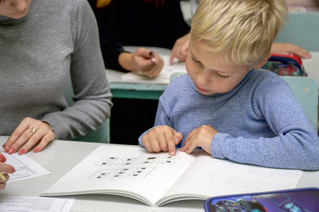 Chapaevsk, Samara region, Russia - October 15, 2019: Elementary school in Chapaevsk. Schoolboy at a desk with a woman teacher. The teacher is engaged with a primary school student. Selective focusのeditorial素材