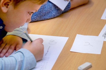 Chapaevsk, Samara region, Russia - October 15, 2019: Elementary school of the city of Chapaevsk. A schoolboy sitting at a desk writes on a sheet of paper. Soft focus. Selective focusのeditorial素材