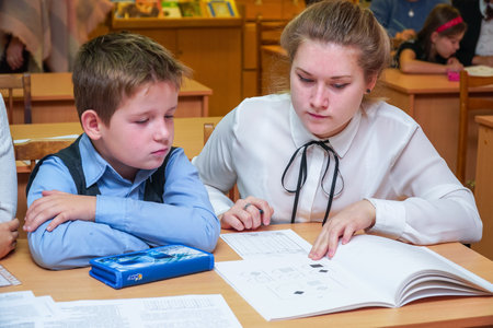 Chapaevsk, Samara region, Russia - October 15, 2019: Elementary school in Chapaevsk. Schoolboy at a desk with a woman teacher. The teacher is engaged with a primary school student. Selective focusのeditorial素材