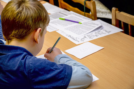 Chapaevsk, Samara region, Russia - October 15, 2019: Elementary school of the city of Chapaevsk. Schoolboy sitting at a desk writes on a sheet of paper. Back view. Soft focus. Selective focusのeditorial素材