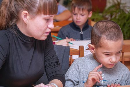 Chapaevsk, Samara region, Russia - October 15, 2019: Elementary school in Chapaevsk. Schoolboy at a desk with a woman teacher. The teacher is engaged with a primary school student. Selective focusのeditorial素材