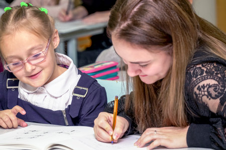 Chapaevsk, Samara region, Russia - October 15, 2019: Schoolgirl in glasses at a desk with a woman teacher. The teacher is engaged with a primary school Schoolgirl. Soft focus. Selective focusのeditorial素材