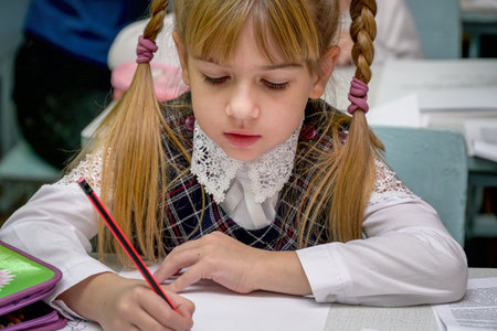 Chapaevsk, Samara region, Russia - October 15, 2019: Elementary school of the city of Chapaevsk. Portrait of a girl with pigtails in the classroom. Schoolgirl writes in a notebookのeditorial素材
