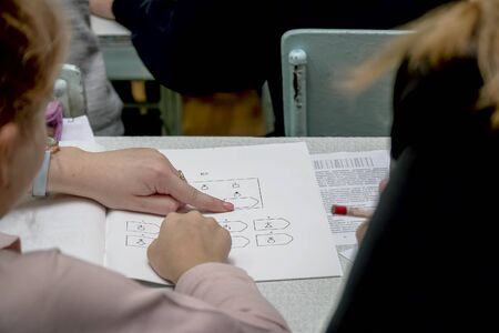The schoolgirl points a finger at the teacher at the figures in the geometry textbook. Selective...