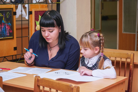 Chapaevsk, Samara region, Russia - October 15, 2019: Schoolgirl at a desk with a woman teacher. The teacher is engaged with a primary school Schoolgirl. Soft focusのeditorial素材