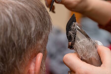 Woman Hairdresser cuts mans hair with electric clipper trimmer. Selective focusの写真素材