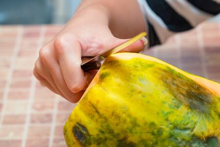 Woman cleans papaya fruit from the peel. Peel the papayaの写真素材
