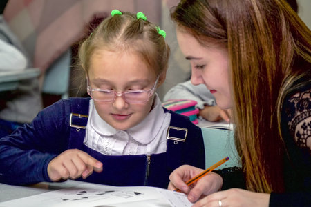 Chapaevsk, Samara region, Russia - October 15, 2019: Schoolgirl in glasses at a desk with a woman teacher. The teacher is engaged with a primary school Schoolgirl. Soft focus. Selective focusのeditorial素材