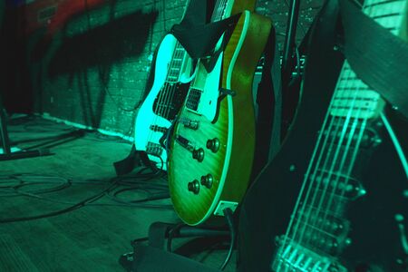 Electric guitars before the concert stand on stage on stands under the light of spotlights.の写真素材