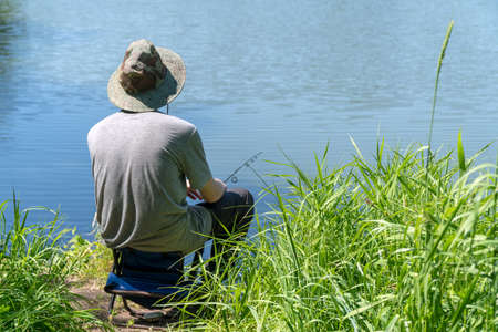 A fisherman in a hat is fishing on a forest lake or riverの写真素材