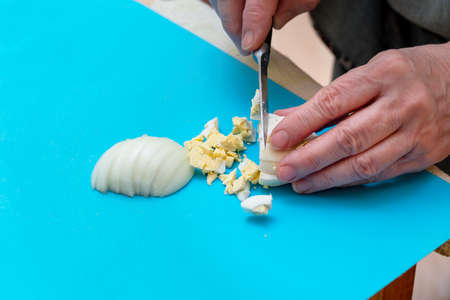 Woman cuts with a knife a white boiled egg on a cutting Board into pieces or slices for saladの写真素材