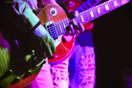 Guitar in the hands of a guitarist standing on stage in the spotlight. Soft focus