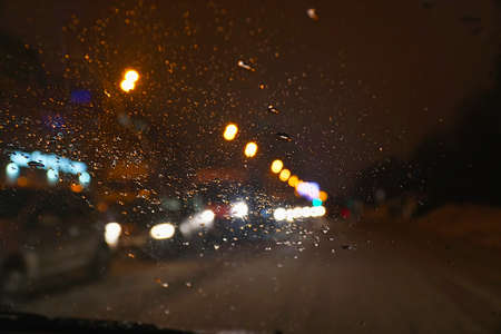 Cars in traffic in winter in the evening dark or at night. View through the windshield, covered with water drops. Blurred viewの写真素材