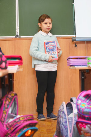 Chapaevsk, Samara region, Russia - December 24, 2020: A primary school schoolgirl stands in the classroom at the blackboard with a book and answers the lessonのeditorial素材