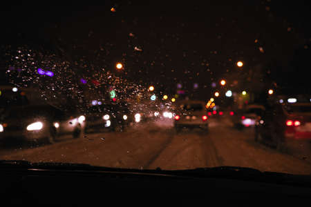 Cars in traffic in winter in the evening dark or at night. View through the windshield, covered with water drops. Blurred viewの写真素材