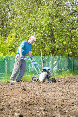 A man cultivates the soil in the garden using a motor cultivator - tillerの写真素材