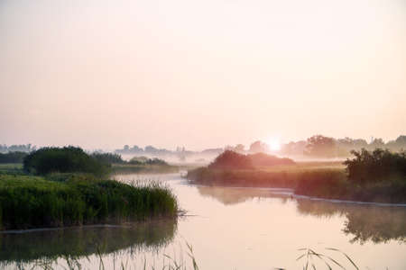 Sunrise in a light fog on a small riverの写真素材