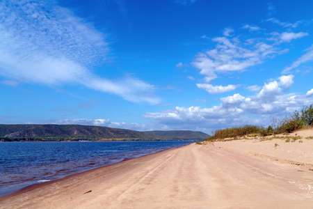 Sandy shore of the big Volga river against the background of a cloudy sky. On the opposite bank of the Zhiguli Mountainsの写真素材