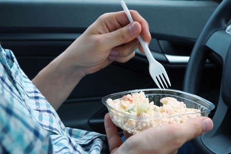 A man, sitting in a car, eats a salad with mayonnaise from plastic disposable dishesの写真素材
