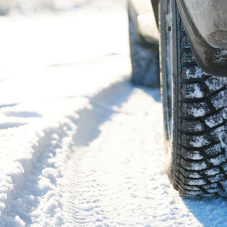 Studded winter car tires on snow-covered road in the sunlightの写真素材
