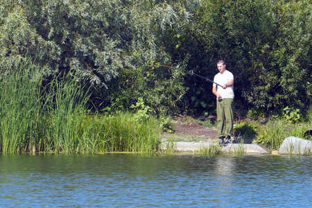 A fisherman on the shore of a lake or river with a fishing rod catches fishの写真素材