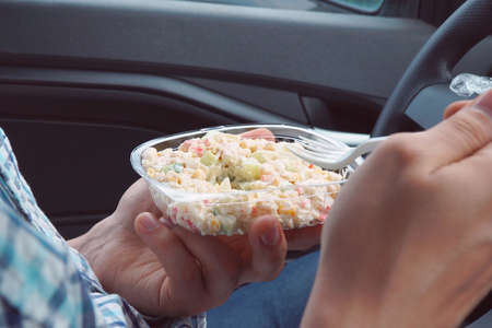 A man, sitting in a car, eats a salad with mayonnaise from plastic disposable dishesの写真素材