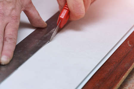 A man cuts a plastic pvc panel with a construction knifeの写真素材