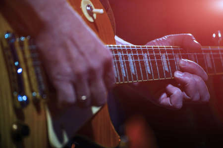 The guitarist plays the guitar in the spotlight. Hands of a Guitar player playing the guitar. Selective focus. Soft focusの写真素材