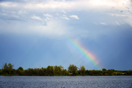 Rainbow in the clouds over the water of a quiet lakeの写真素材