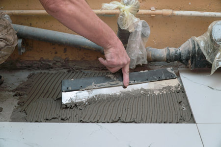 A construction worker applies cement for laying floor ceramic tiles with a special spatulaの写真素材