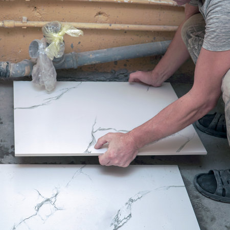 A male builder tiler lays floor ceramic tiles. Selective soft focusの写真素材