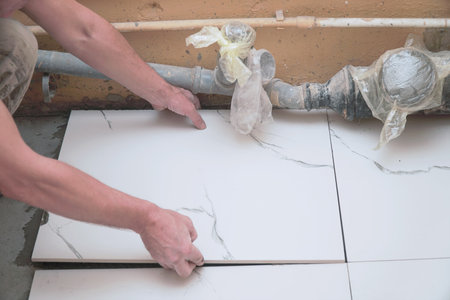 A male builder tiler lays floor ceramic tiles. Selective soft focusの写真素材