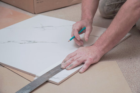 The hands of a man marking ceramic floor tiles with a ruler and pencil for laying on the floor. Selective focus. Soft focusの写真素材