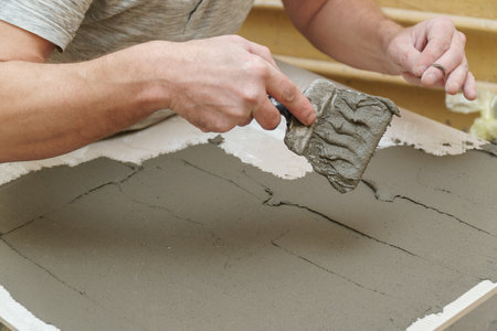 A construction worker applies cement to a ceramic tile with a spatula. Selective focus