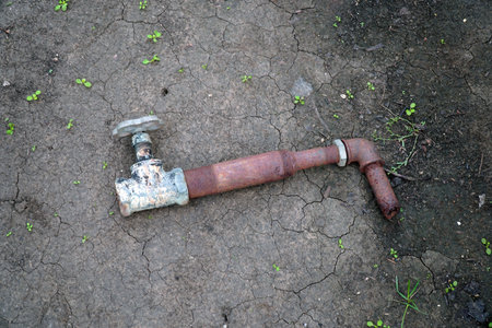 A fragment of an old rusty pipe with a tap on the ground