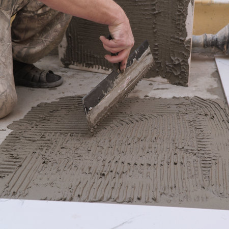 A construction worker applies cement for laying floor ceramic tiles with a special spatulaの写真素材