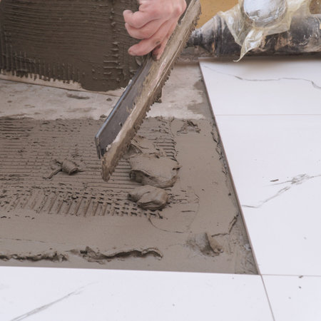 Hand Applying Tile Adhesive for Flooring Installation. Hand using a trowel to apply tile adhesive mortar on floor surface, preparing for tile installationの写真素材